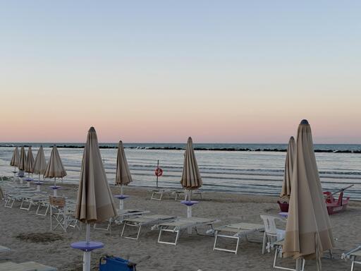 Spiaggia vuota con sedie e ombrelloni, mare tranquillo e cielo al tramonto.