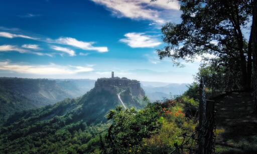 Civita di Bagnoregio con vista sulle montagne e il cielo azzurro, circondato da vegetazione e alberi.